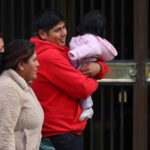 Crisis de natalidad: Gobierno da suma urgencia a dos proyectos de fertilidad Un hombre con polerón rojo sonríe mientras sostiene en brazos a un bebé con chaqueta rosada.