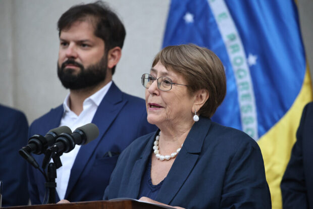 Michelle Bachelet hablando en un punto de prensa. Detrás se ve la bandera de Brasil y al expresidente Boric.