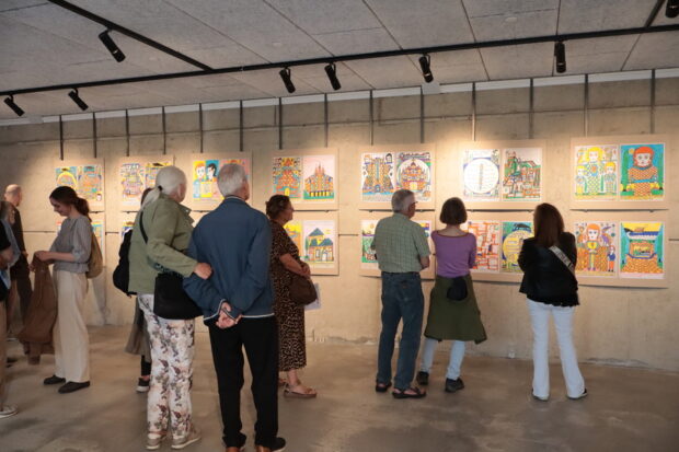 Vista trasera de un grupo de personas observando una exposición de cuadros de arte.