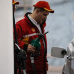 Un trabajador de la Shell se ve sosteniendo la manguera de combustible mientras carga bencina a un vehículo.