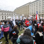 Confusam entrega carta a Kast en rechazo a los recortes de la Atención Primaria: manifestación termina con detenidos Funcionarios de la Atención Primaria de Salud de manifiestan frente a La Moneda entre banderas de Chile y con el logo de la organización.