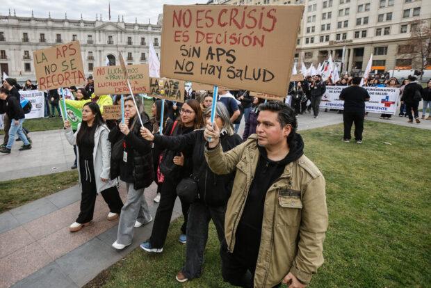 Manifestación de funcionarios de la Atención Primaria de Salud frente a La Moneda, con carteles que dicen "No es crisis, es decisión. Sin APS no hay salud".