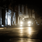 Auto con luces encendidas transita por una calle oscura.