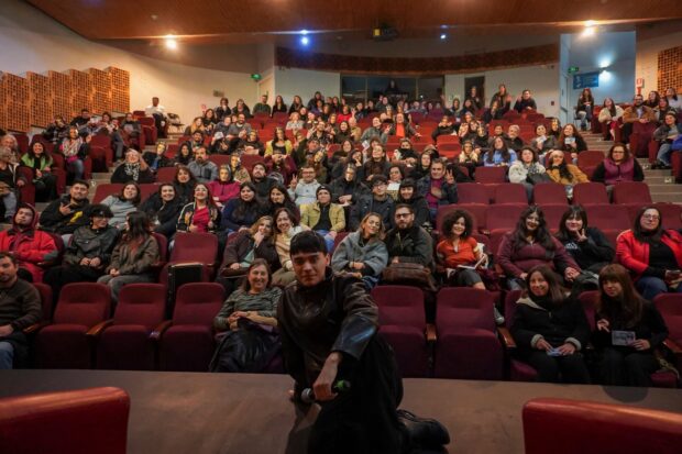 Matías Catalán sentada en un escenario, detrás de él se ve un auditorio con sillas rojas y decenas de personas sentadas. Todos posan para la foto.