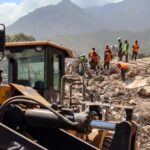 Asciende a 5 mil 119 la cifra de fallecidos por los terremotos en Venezuela Una excavadora amarilla en primer plano. Detrás se ve un equipo de rescatistas con cascos y chalecos de seguridad mientras buscan entre los escombros de un edificio derrumbado.
