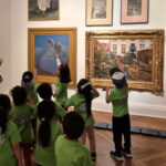 Ponencias y experiencias sobre educación artística se presentarán en el VIII Seminario Internacional de Investigaciones sobre Arte y Educación Niños pequeños vestidos con polera verde se ven de espaldas mientras miran cuadros de arte en una exposición.