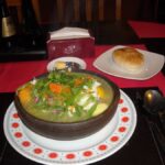 Centro de Santiago celebra el Día de la Cazuela en restaurantes y locales tradicionales del casco histórico Cazuela chilena servida en un pocillo de greda con verduras, carne y pan sobre la mesa de un restaurante.