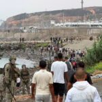Decenas de migrantes regresan caminando a Marruecos mientras son vigilados por militares españoles.