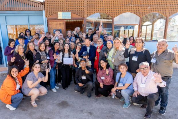 Grupo de dirigentes y dirigentas sociales posa frente a un edificio comunitario, levantando las manos durante una actividad de la División de Organizaciones Sociales.