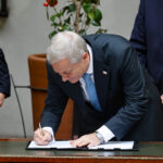 Presidente Kast firmando un documento sobre una mesa de madera.