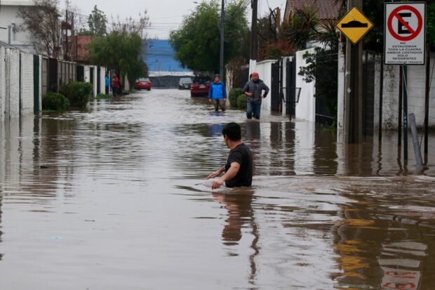 Hombre en medio de una calle residencial inundada. El agua le llega hasta la mitad del pecho.