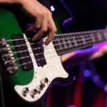 ¿Y la música no sirve para nada? Plano detalle de un bajo verde y blanco. En la foto se ven unas manos tocando notas en él.