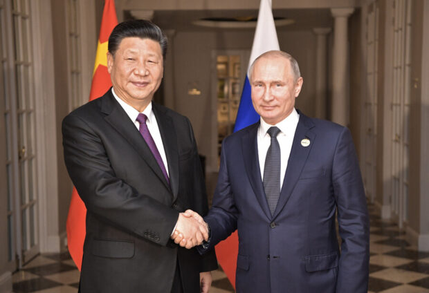 El presidente ruso, Vladimir Putin, y su par de China, Xi Jiping, posan para una foto mientras se estrechan la mano. Detrás de ellos la bandera de China y Rusia.
