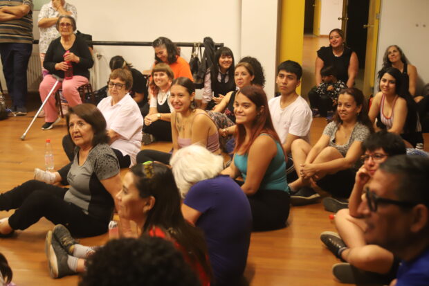 Personas sentadas en el suelo de una sala de ensayos.